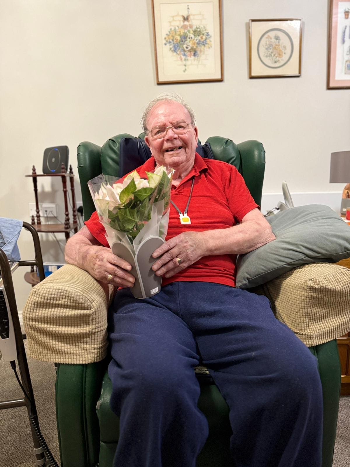An elderly man sitting in a cozy armchair smiles broadly while holding a bouquet of flowers, exemplifying the joy of receiving thoughtful gestures during the holiday season. Surrounded by a warm and inviting living space, this image highlights the importance of Christmas care and elderly care, showcasing how companionship and small acts of kindness can enhance the well-being of seniors. The cheerful atmosphere reflects the spirit of care and connection that makes the holidays special for older adults.