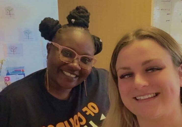Two women smiling together in an office setting, highlighting the importance of teamwork in Alzheimer's care.