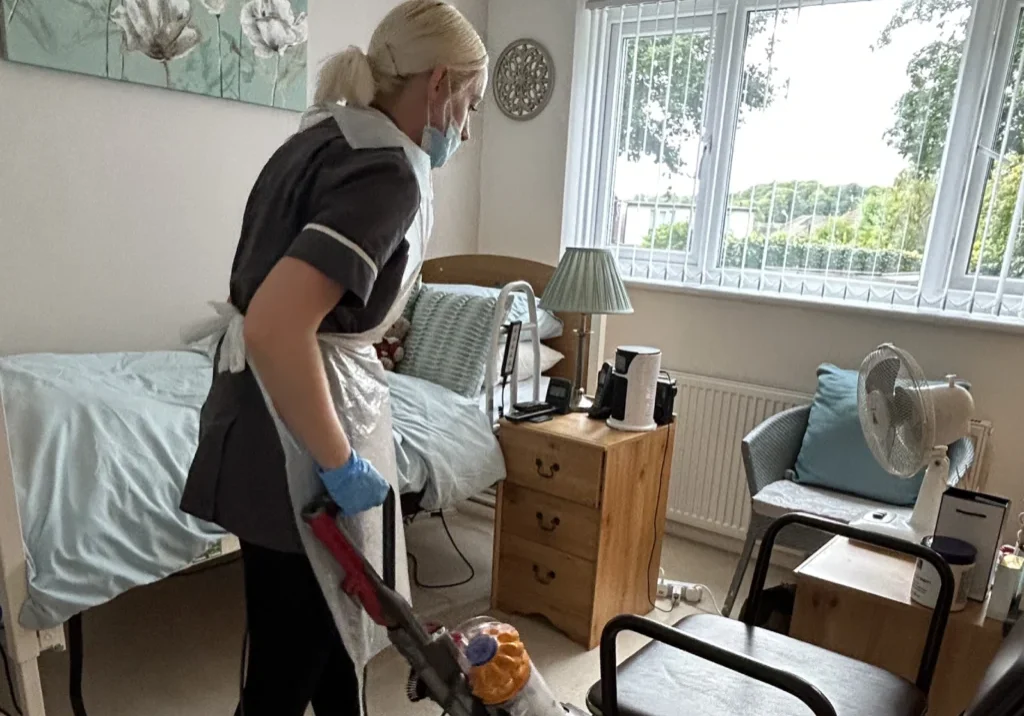 A caregiver cleaning a room while wearing gloves and a mask, highlighting the importance of jobs in care for maintaining hygiene and comfort