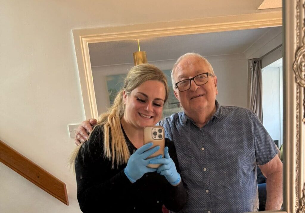 A caregiver smiling with an elderly man in a cozy living room, reflecting the supportive relationship fostered through compassionate care.